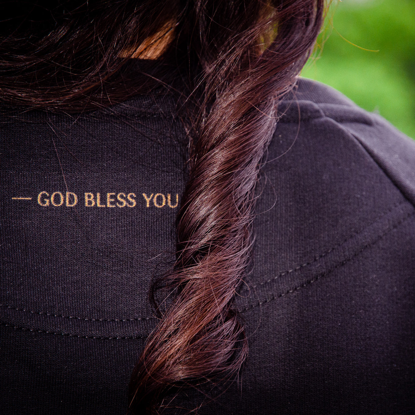 Nackenpartie eines schwarzen Sweatshirts mit dem Aufdruck GOD BLESS YOU in gold
