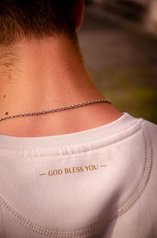 Rückseite eines cremeweißen Sweatshirts mit goldenem GOD BLESS YOU Druck im Nackenbereich.