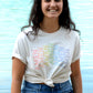 UnisexFrau trägt cremeweißes T-Shirt mit AMEN Druck in Regenbogenfarben