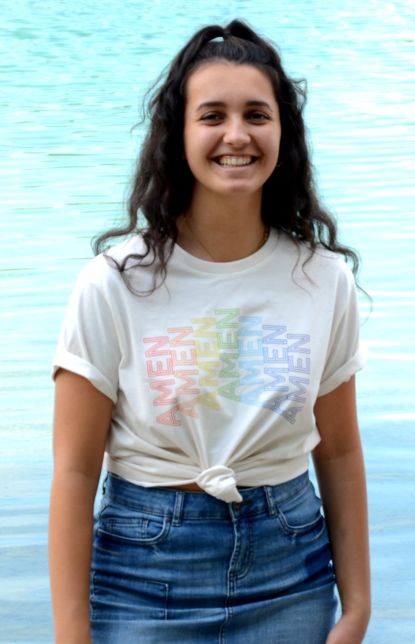 UnisexFrau trägt cremeweißes T-Shirt mit AMEN Druck in Regenbogenfarben